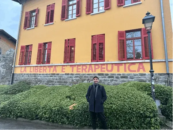 Cristian Montenegro standing in front of the mural 'La Libertá e Terapeutica' at the San Giovanni Psychiatric Hospital, Trieste