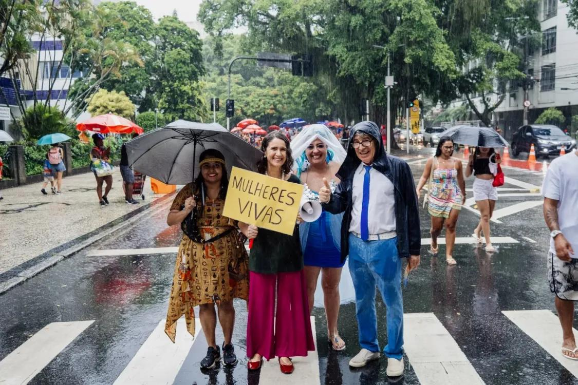 Three women and a man, standing in the rain, with a sign saying Mulheres Viva