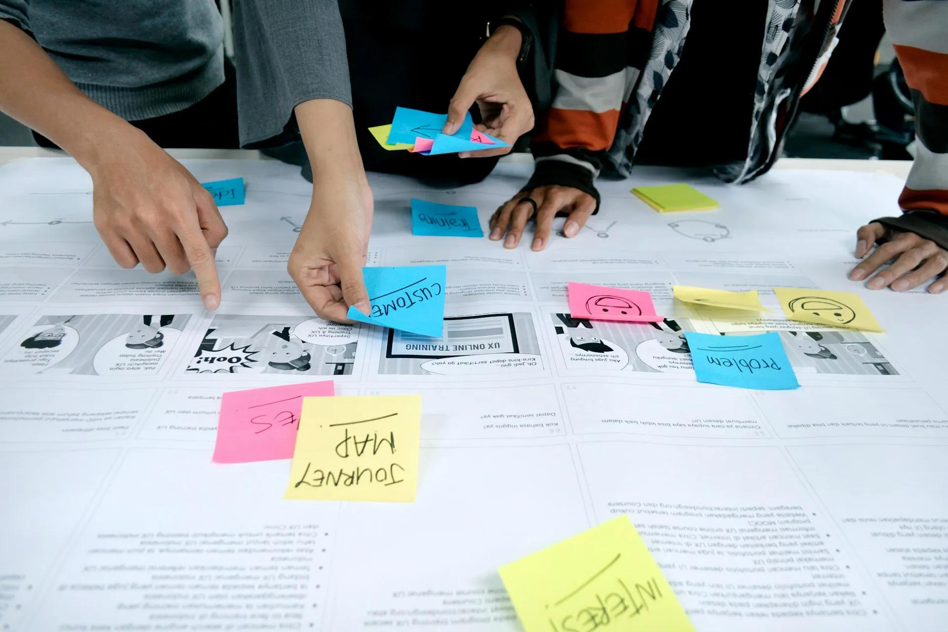 The hands of several people placing post-it notes on documents lying on a table